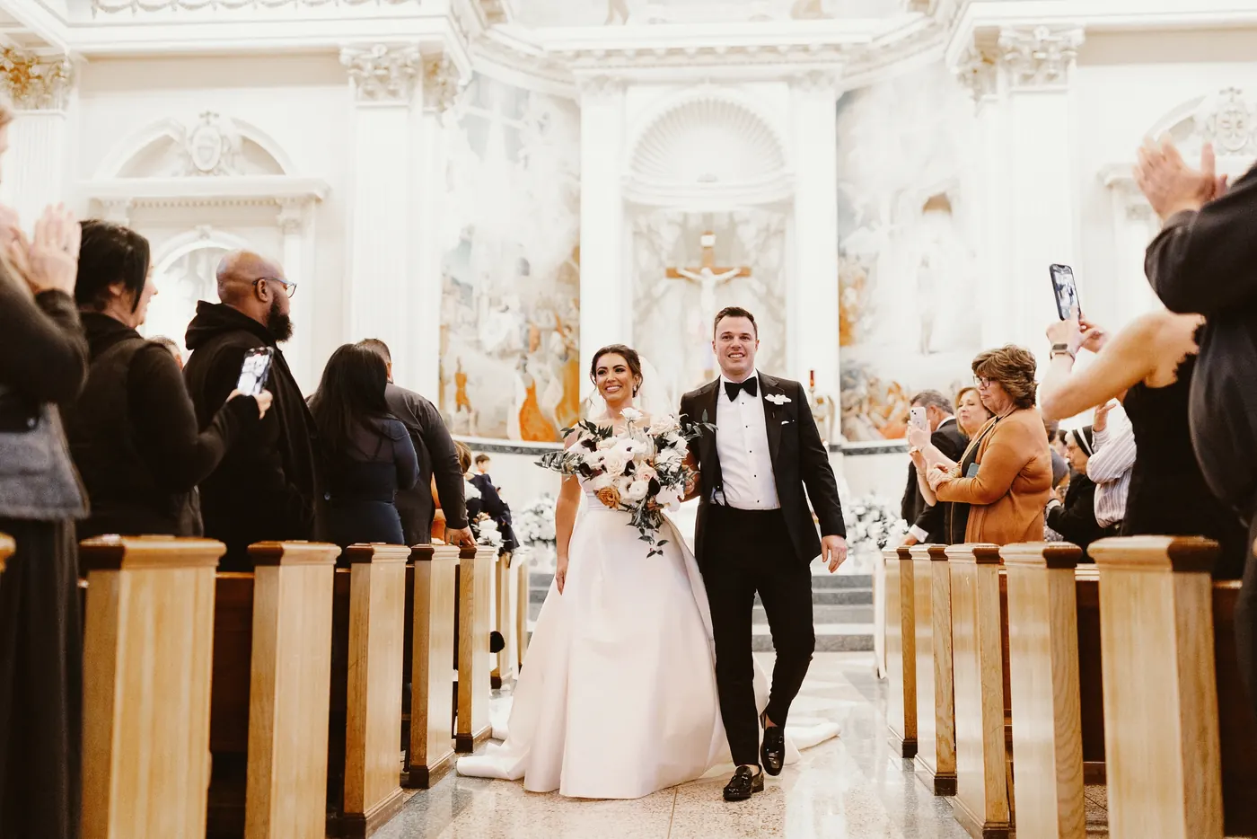 Guests cheering as Branon and Celeste walk back up the aisle during their ceremony at Saint Monica Roman Catholic Church in South Philadelphia