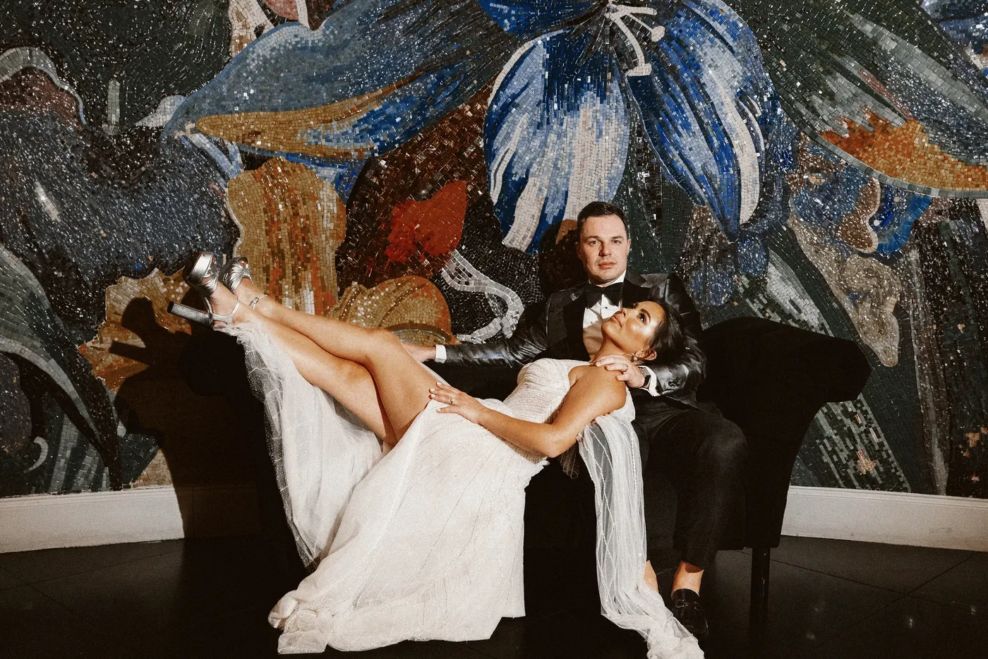 Branon and Celeste on a black velvet chaise in front of a colorful floral mosaic at The Vie by Cescaphe in Philadelphia