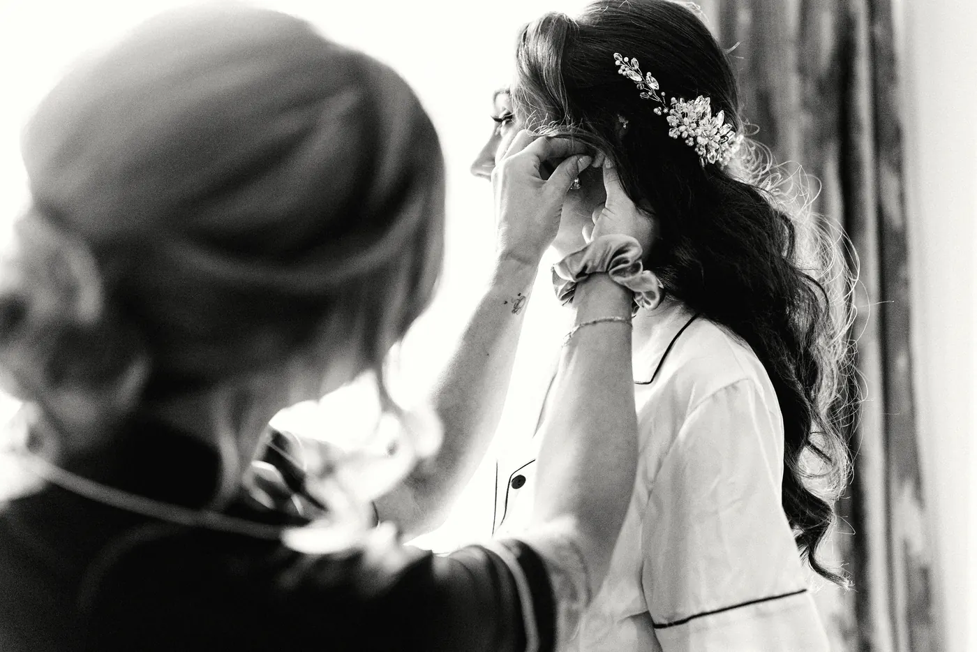 Black and white photo of Danielle putting on her earrings as her hair is finished