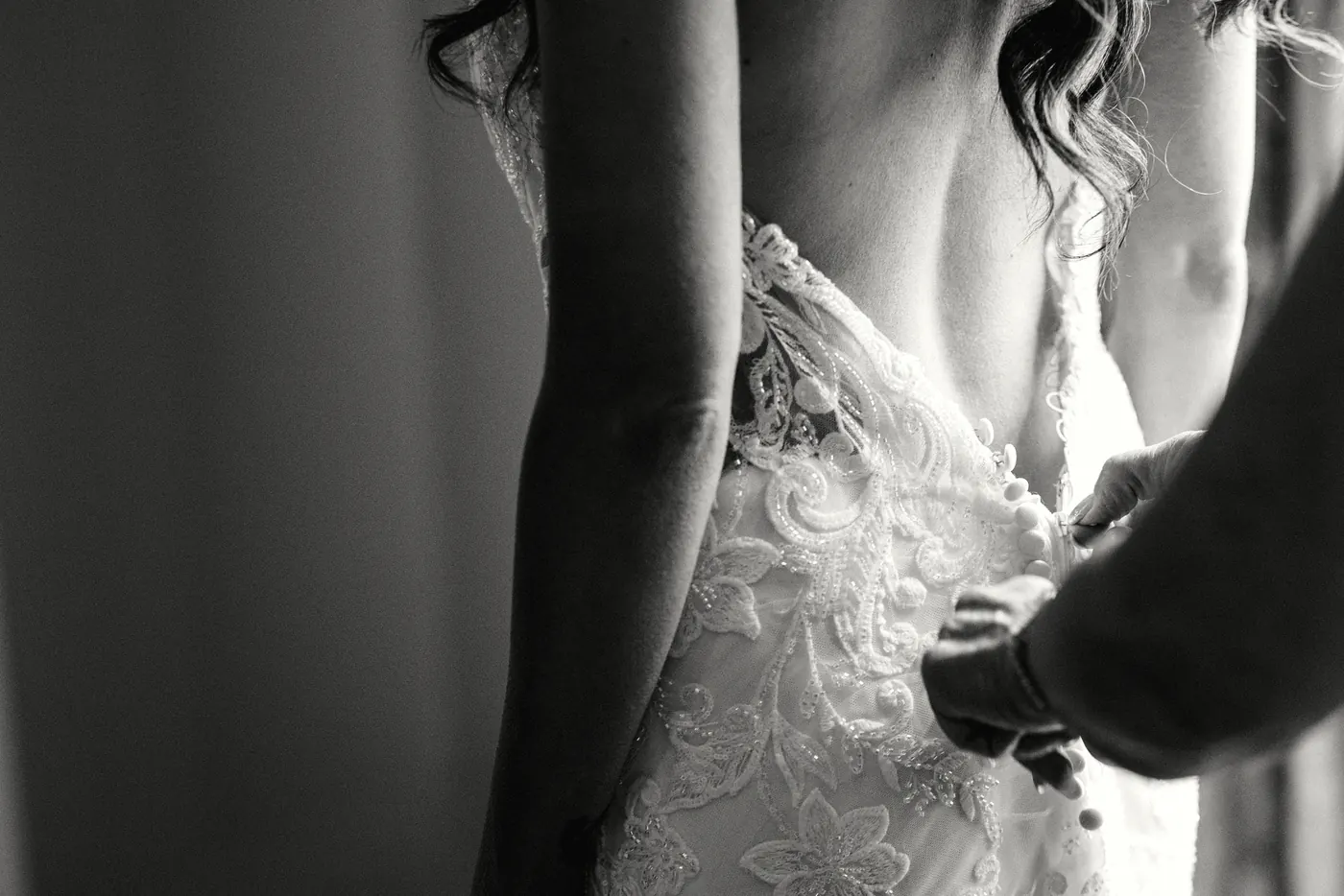 Black and white close-up of Danielle's lace wedding dress being buttoned