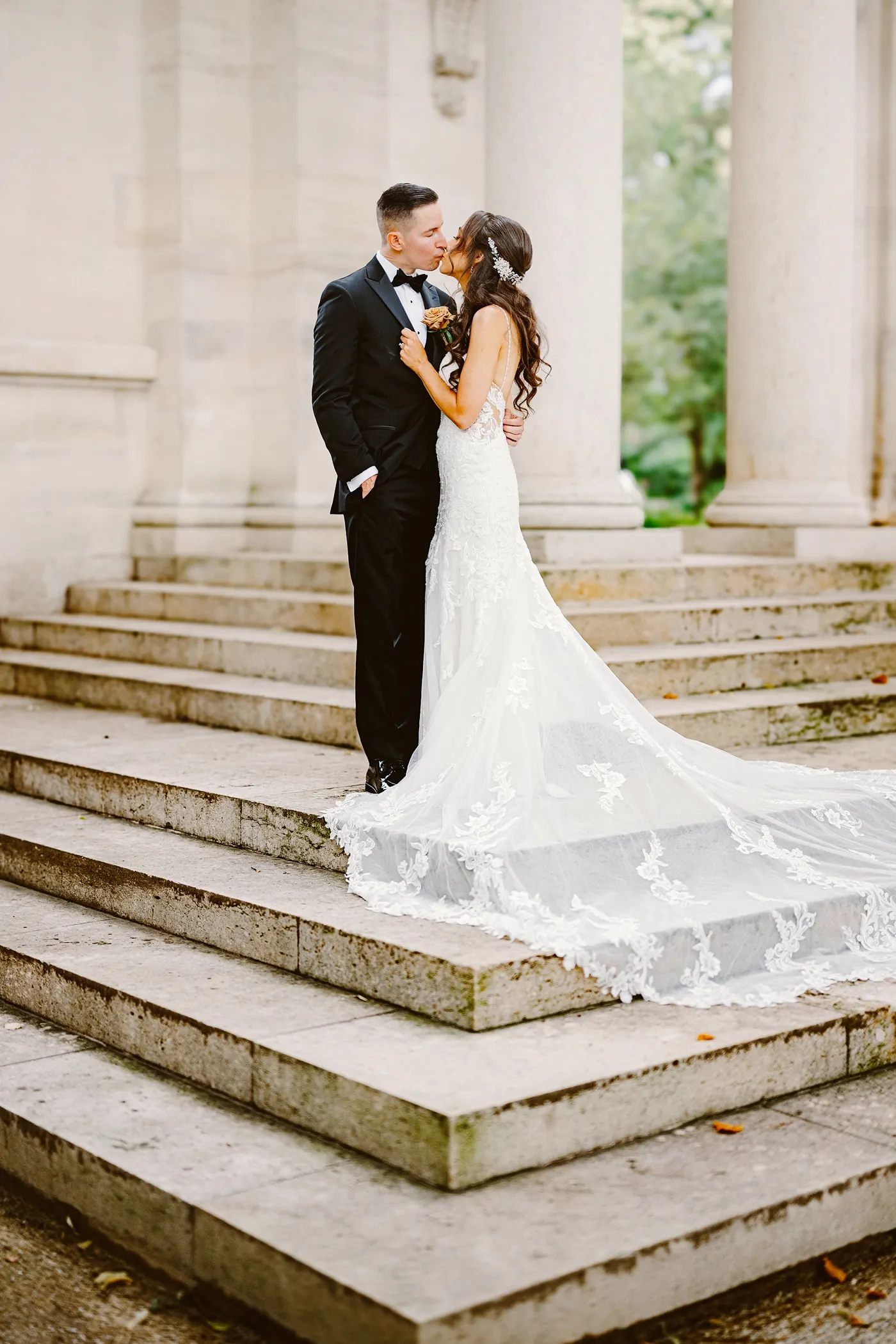 Chris kissing Danielle on the museum steps with her long train below at the Rodin Museum in Philadelphia