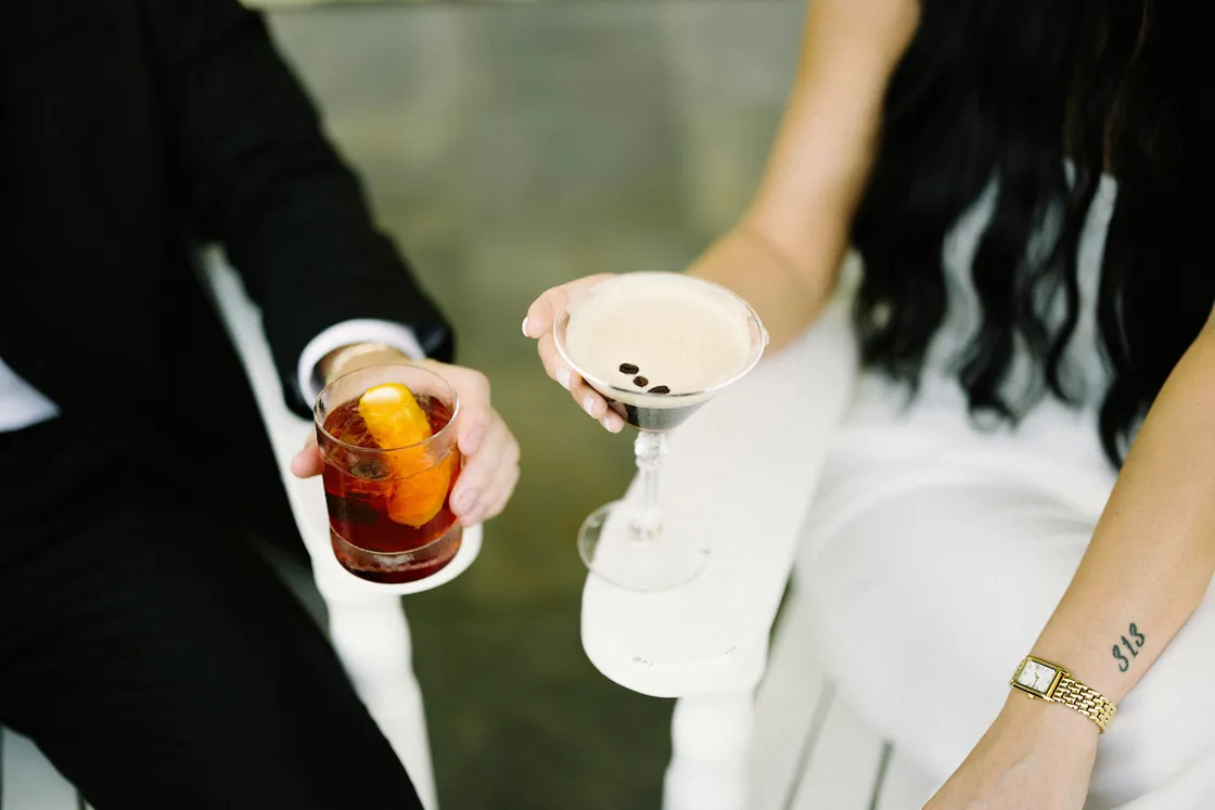 Mason and Morgan holding an old fashioned and an espresso martini on the porch of Congress Hall in Cape May, NJ, during their engagement session