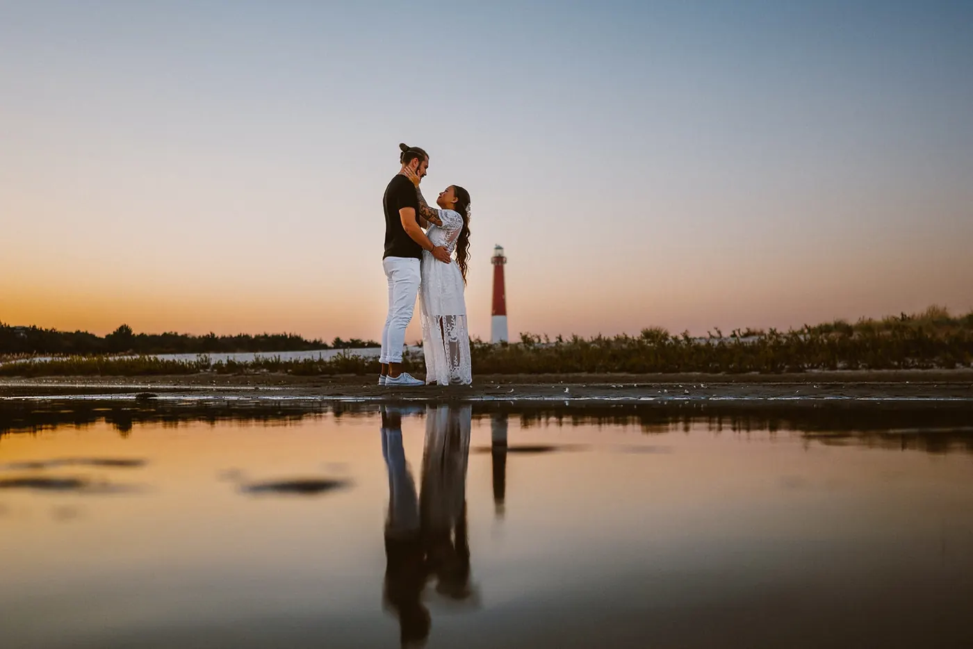 Dan and Madison reflected in the water with Barnegat Lighthouse behind them at sunset