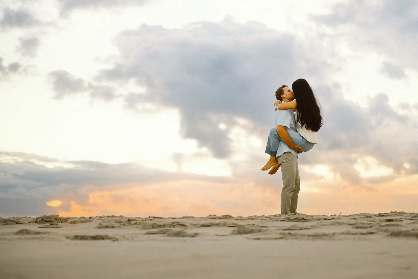 Mason lifting Morgan under dramatic clouds at sunset in Cape May, NJ, near Congress Hall