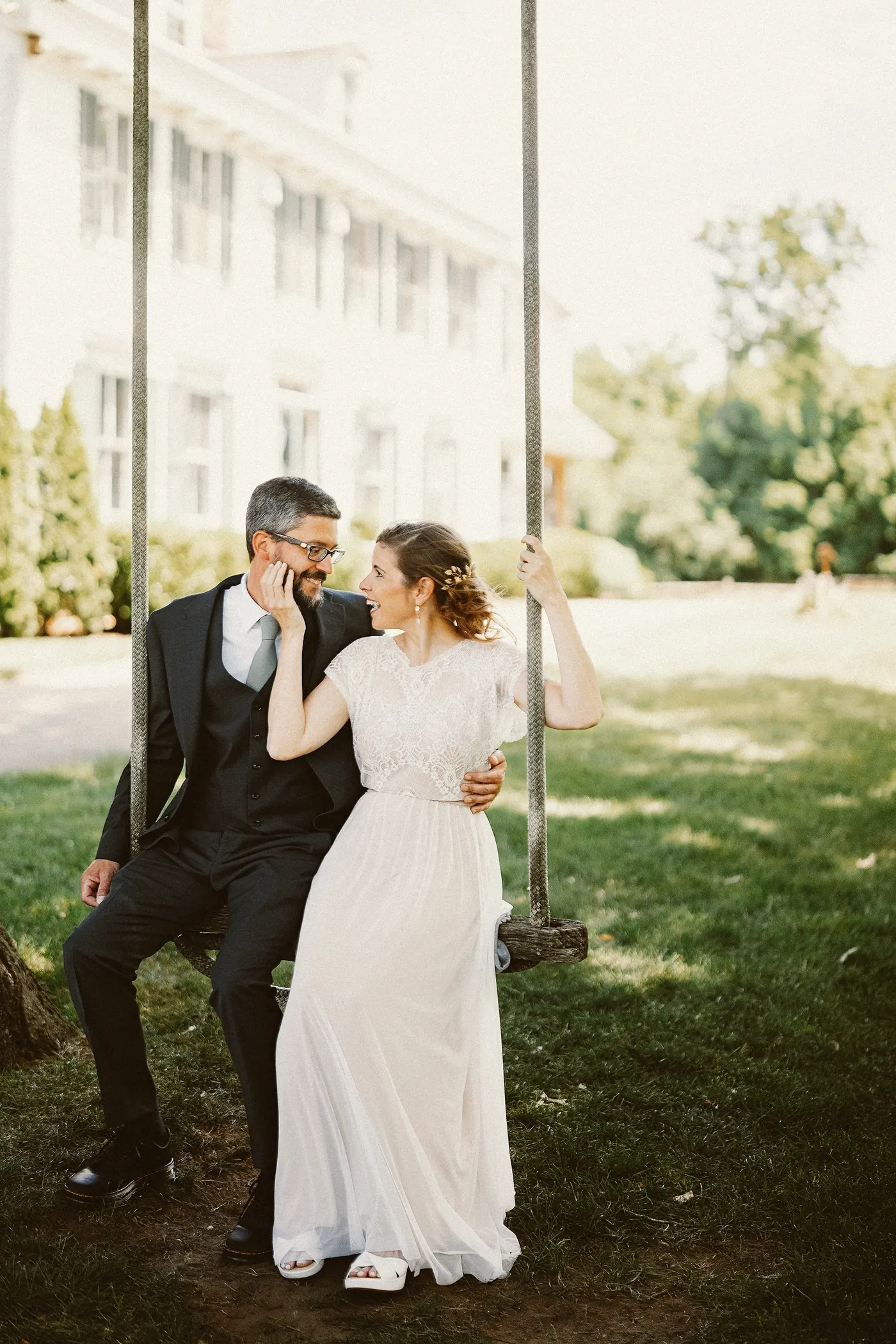 Matt and Erica laughing together on a rope swing in front of the farmhouse at Johnson's Locust Hall Farm in Jobstown, NJ