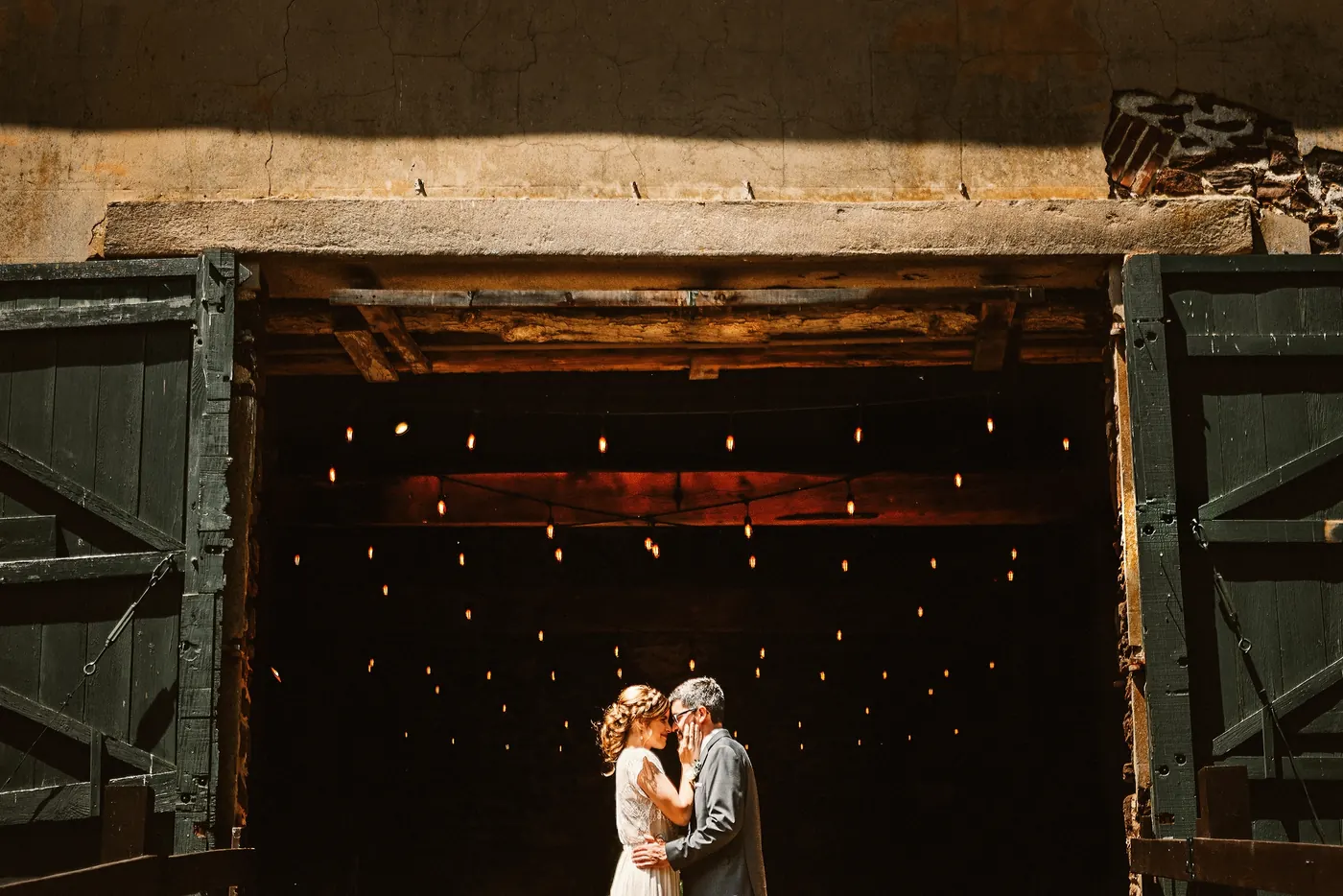 Matt and Erica in the open barn doors with string lights glowing behind them at Johnson's Locust Hall Farm in Jobstown, NJ