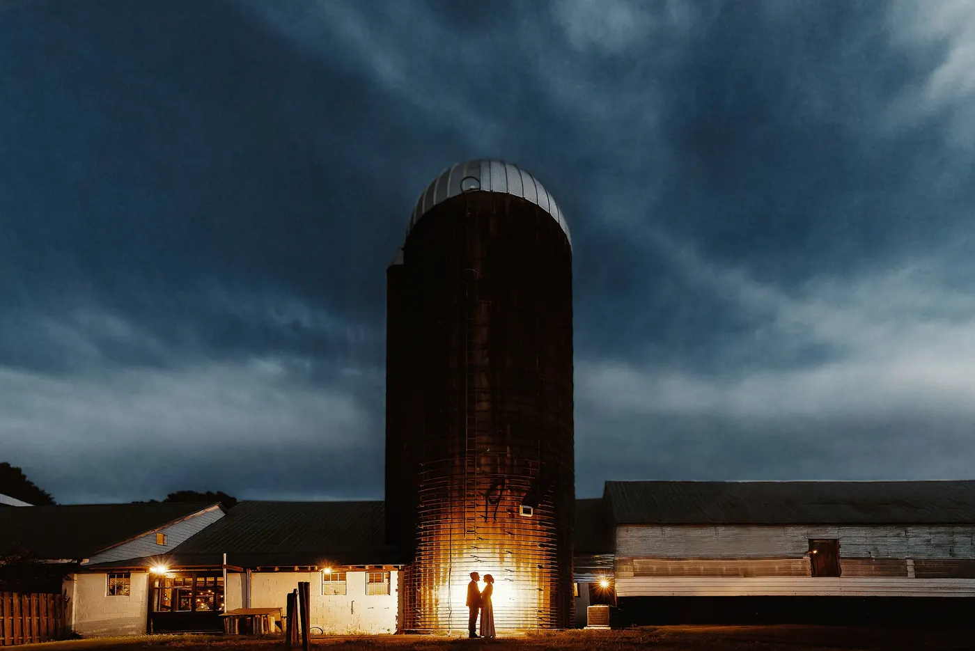 Matt and Erica silhouetted by the glowing silo under a stormy night sky at Johnson's Locust Hall Farm in Jobstown, NJ
