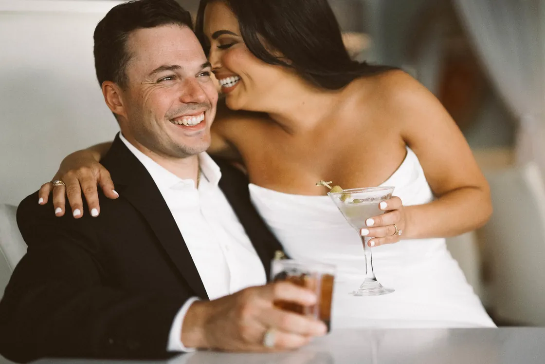 Branon and Celeste laughing together over cocktails during their Ocean City, NJ engagement session near the Longport bridge