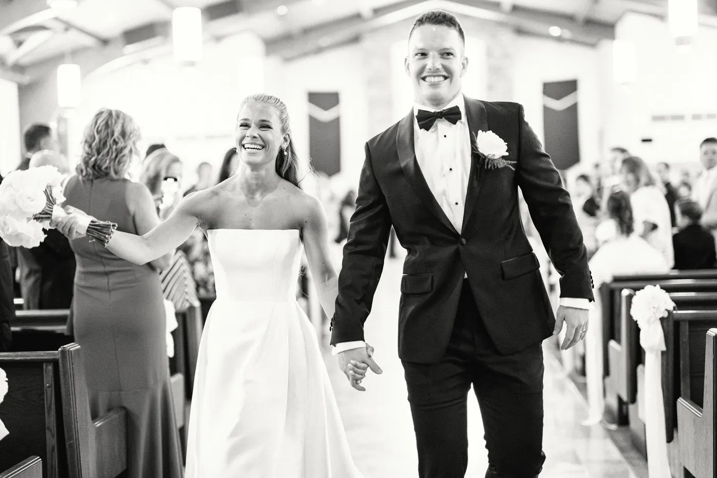 Steve and Madison smiling as they walk back down the aisle as newlyweds, in black and white
