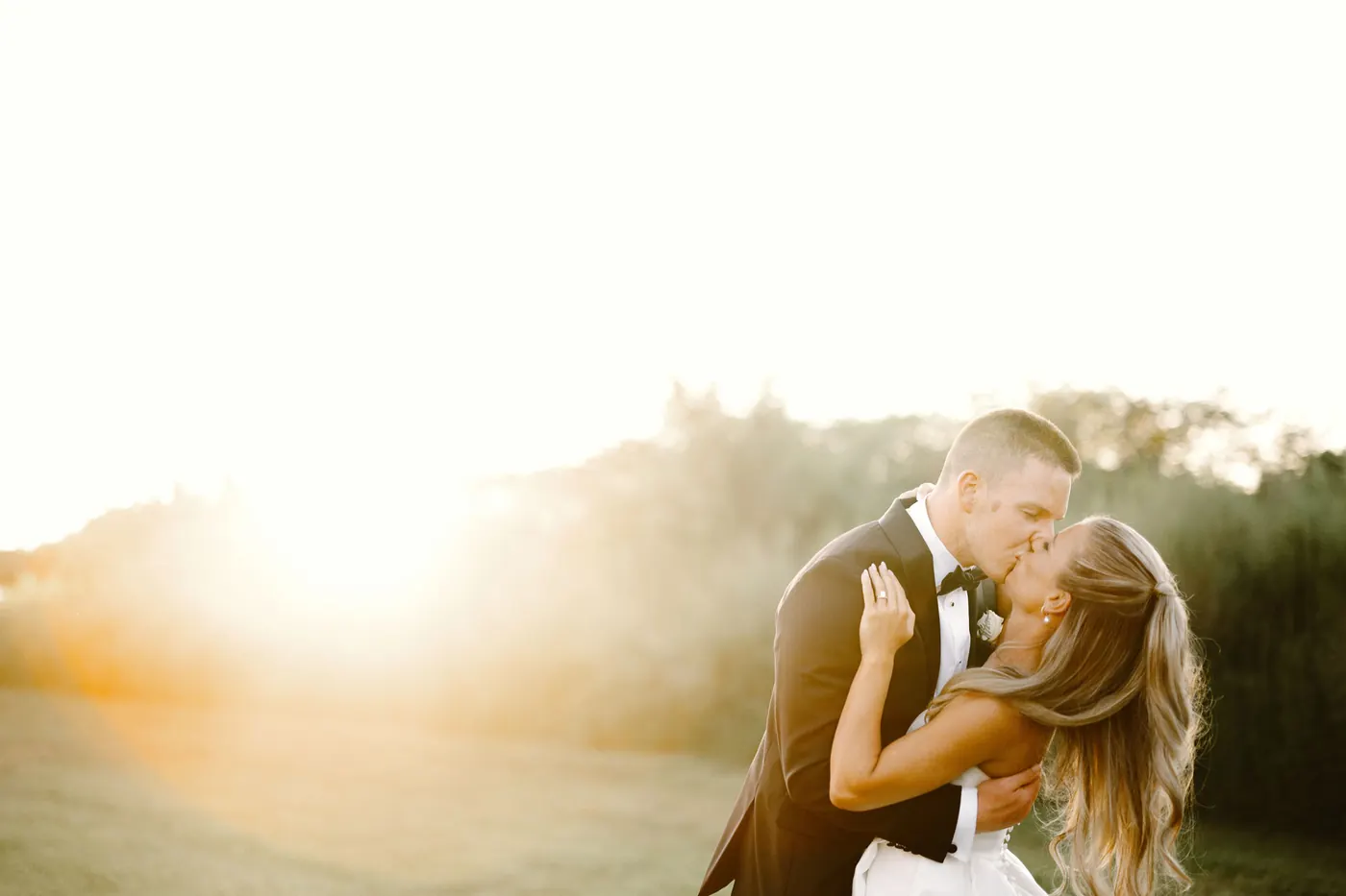 Steve and Madison kissing in golden sunset light at their Bishop Farmstead barn wedding