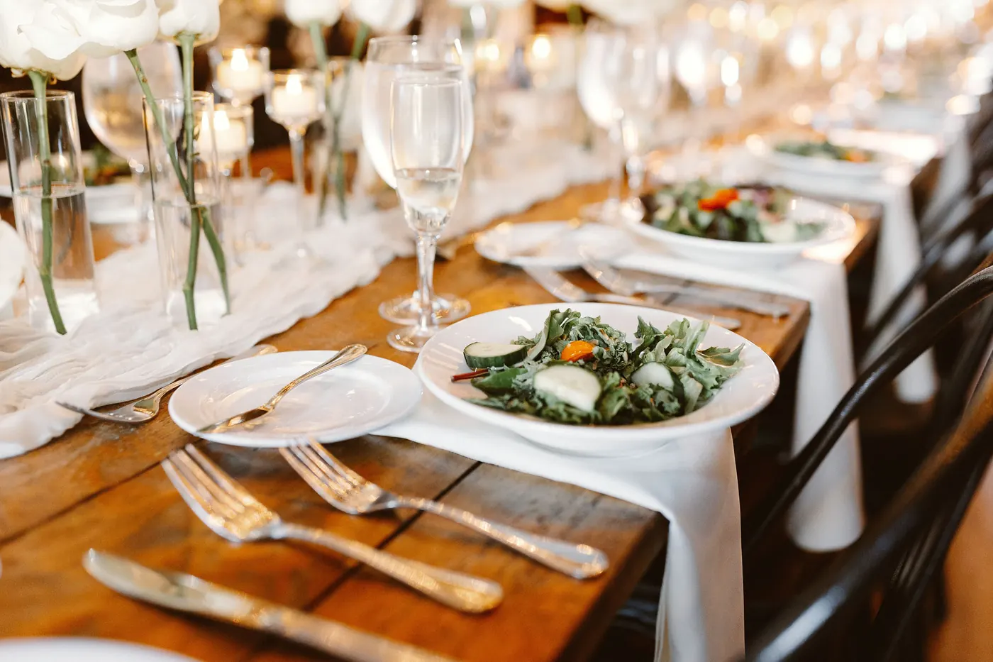 A reception place setting with salad, glassware and white linen