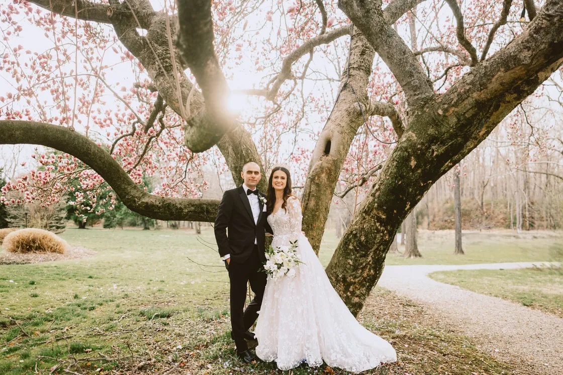 Steve and Maria standing beneath a blooming magnolia tree at their Woolverton Inn wedding